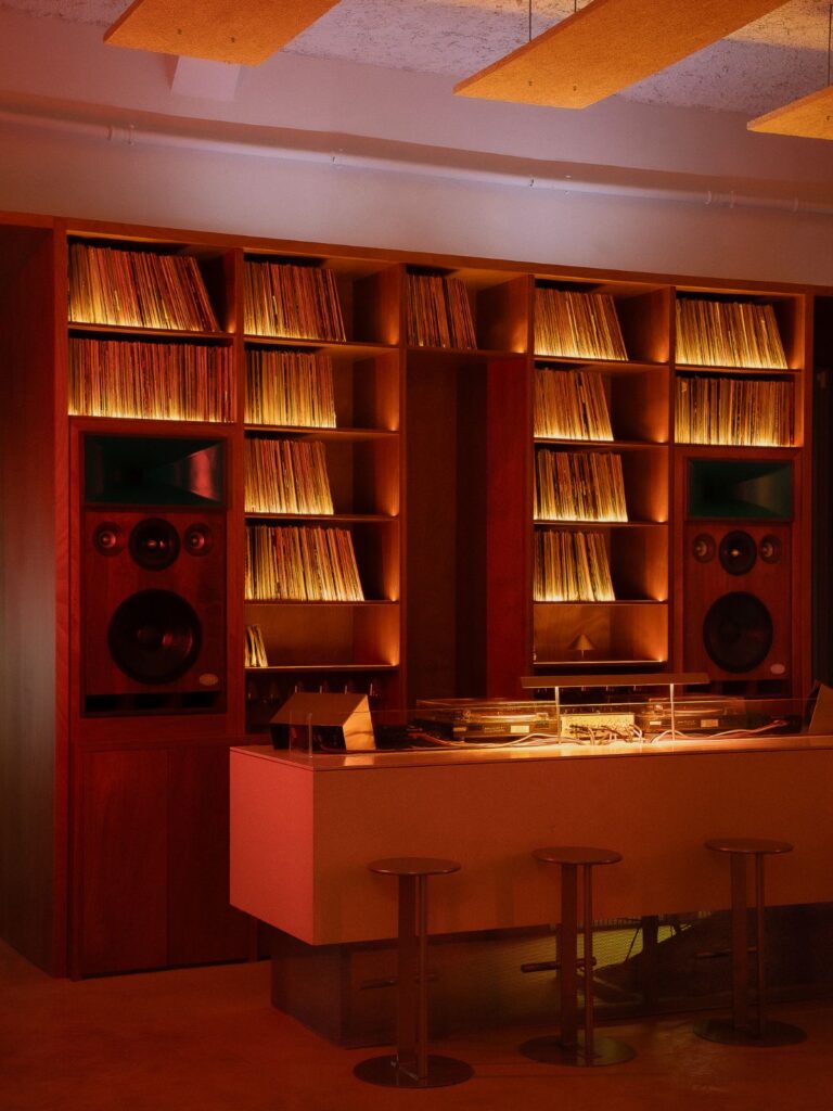 Parete di vinili retroilluminata con due diffusori hi-fi integrati e consolle sotto pannelli acustici sospesi da Frissón a Roma