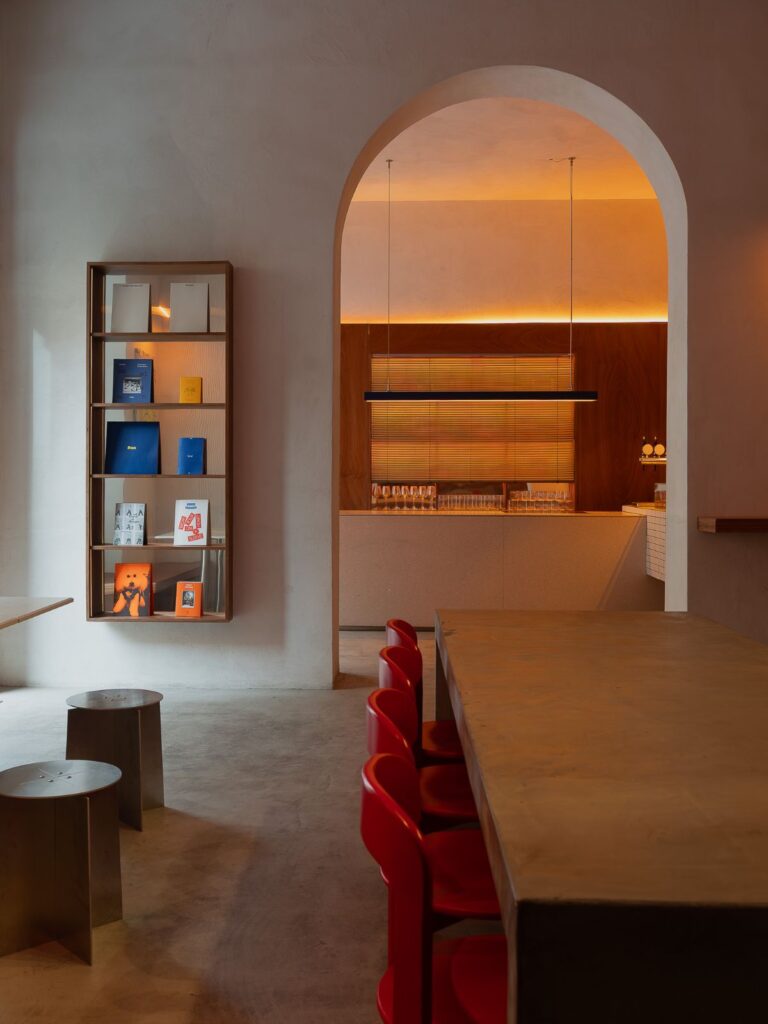 Sala di Frissón con tavolo conviviale, sedute rosse, libreria a parete e bar inquadrato dall'arco