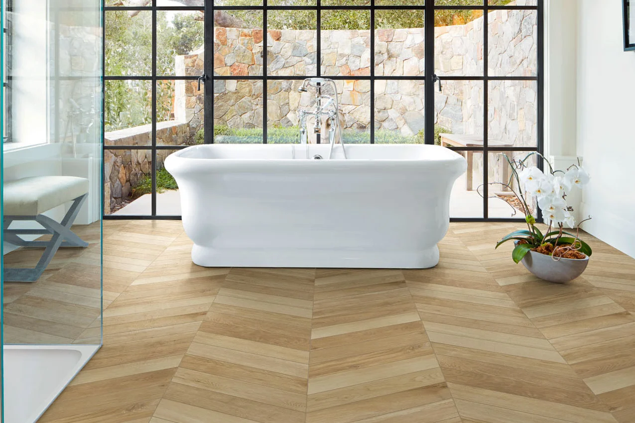Bagno con vasca freestanding e vetrata sul giardino con pavimento in gres effetto legno posato a spina francese
