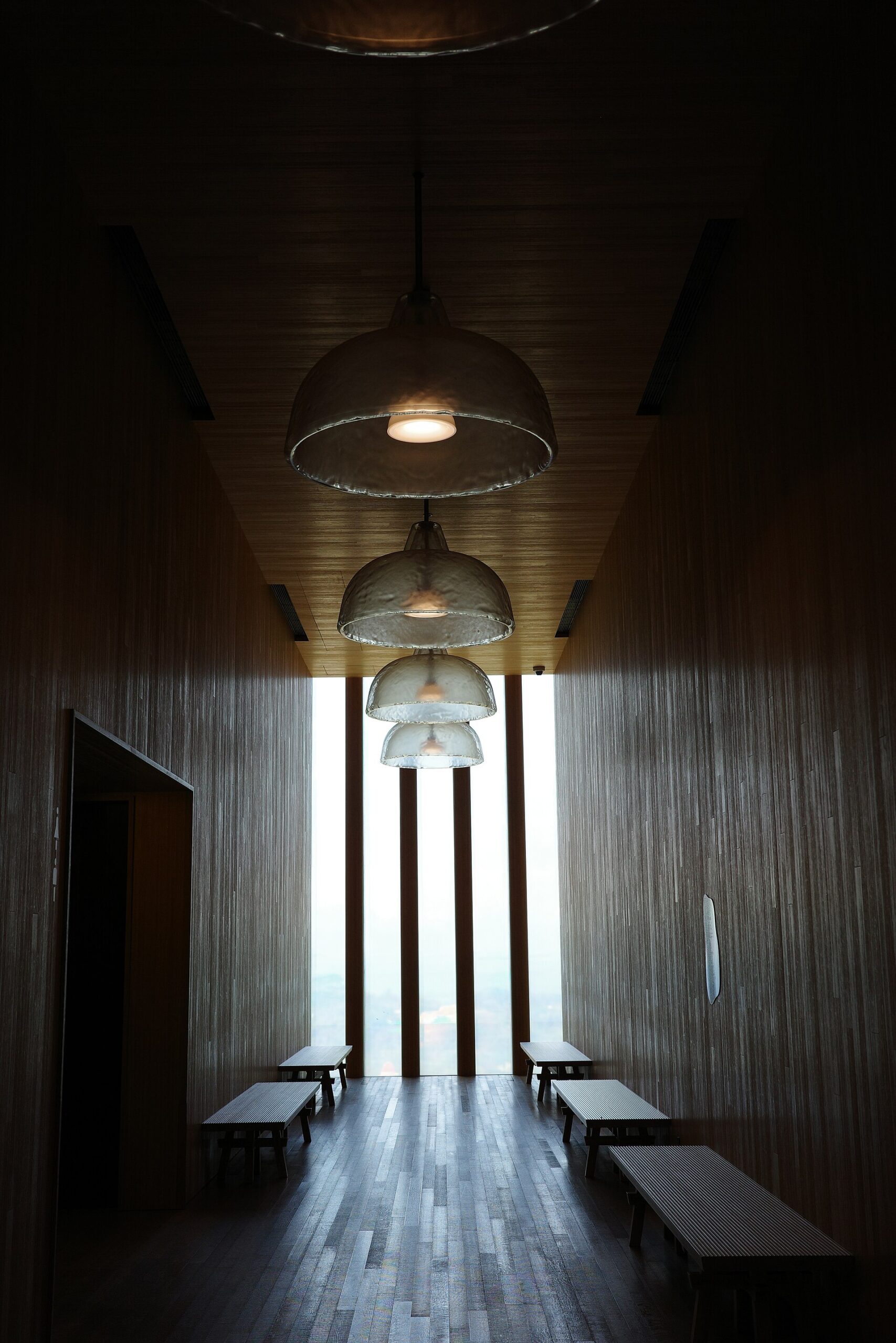 Panche e lampade sospese in un corridoio rivestito in legno del museo M+