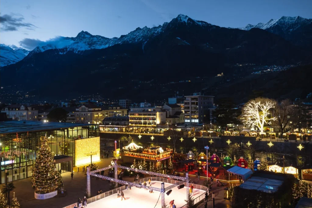 Piazza Terme in Merano at Christmas with the ice rink and the mountains at dusk