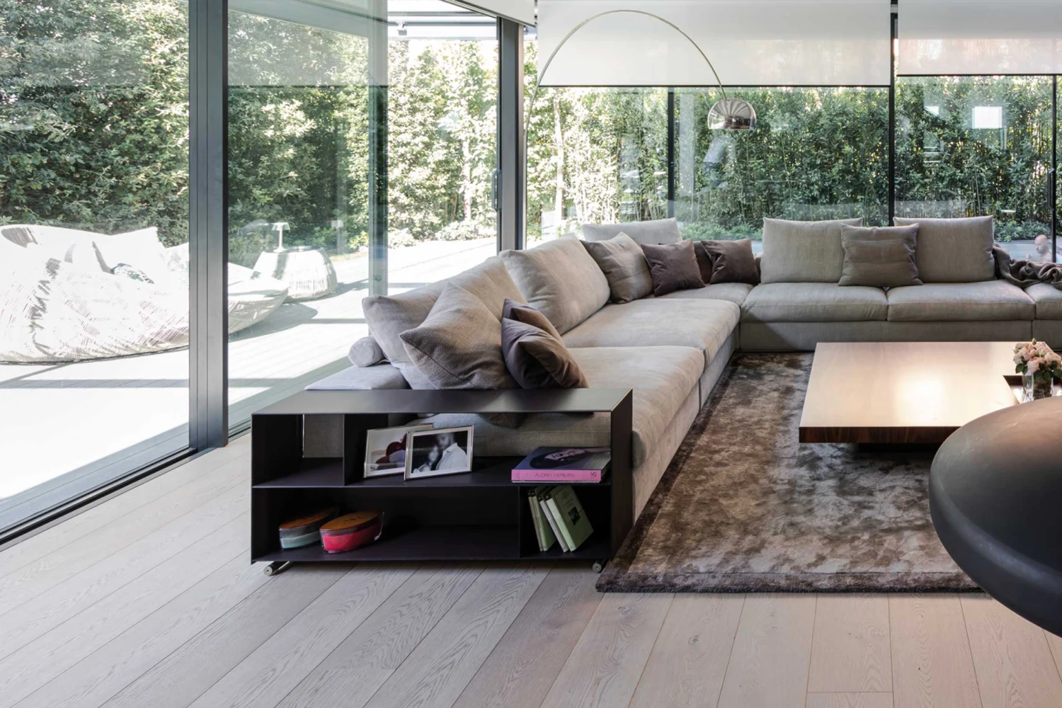 Soggiorno con divano grigio e grandi vetrate sul giardino con parquet chiaro a plance larghe
