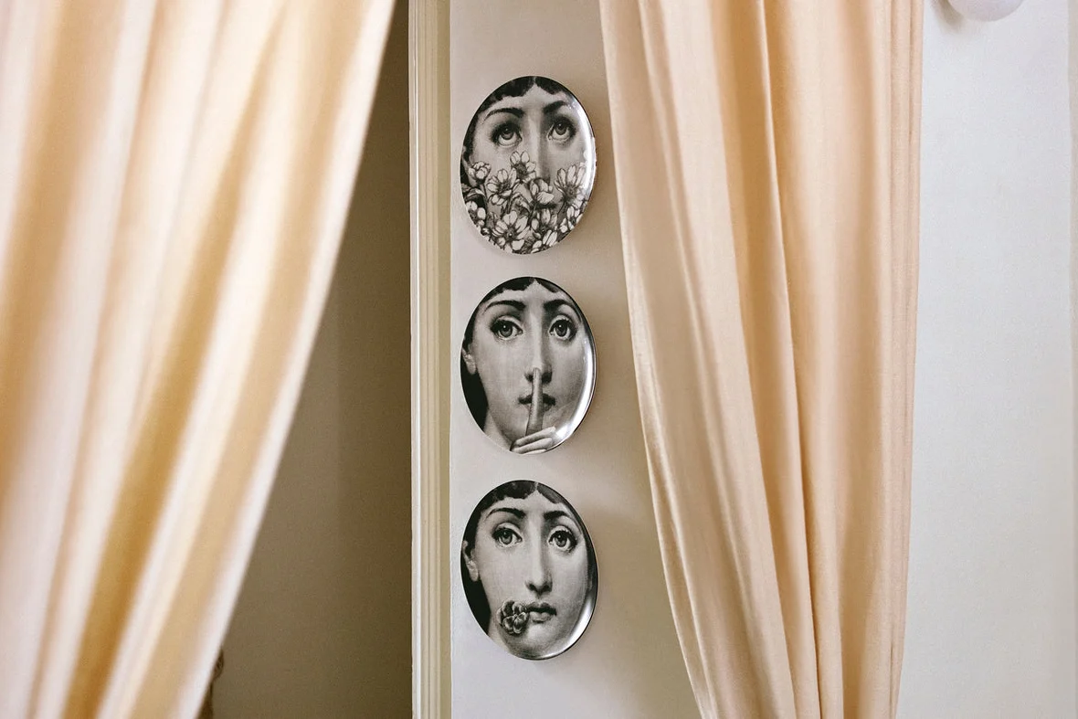 Fornasetti Tema e Variazioni plates hung on a wall between two curtains
