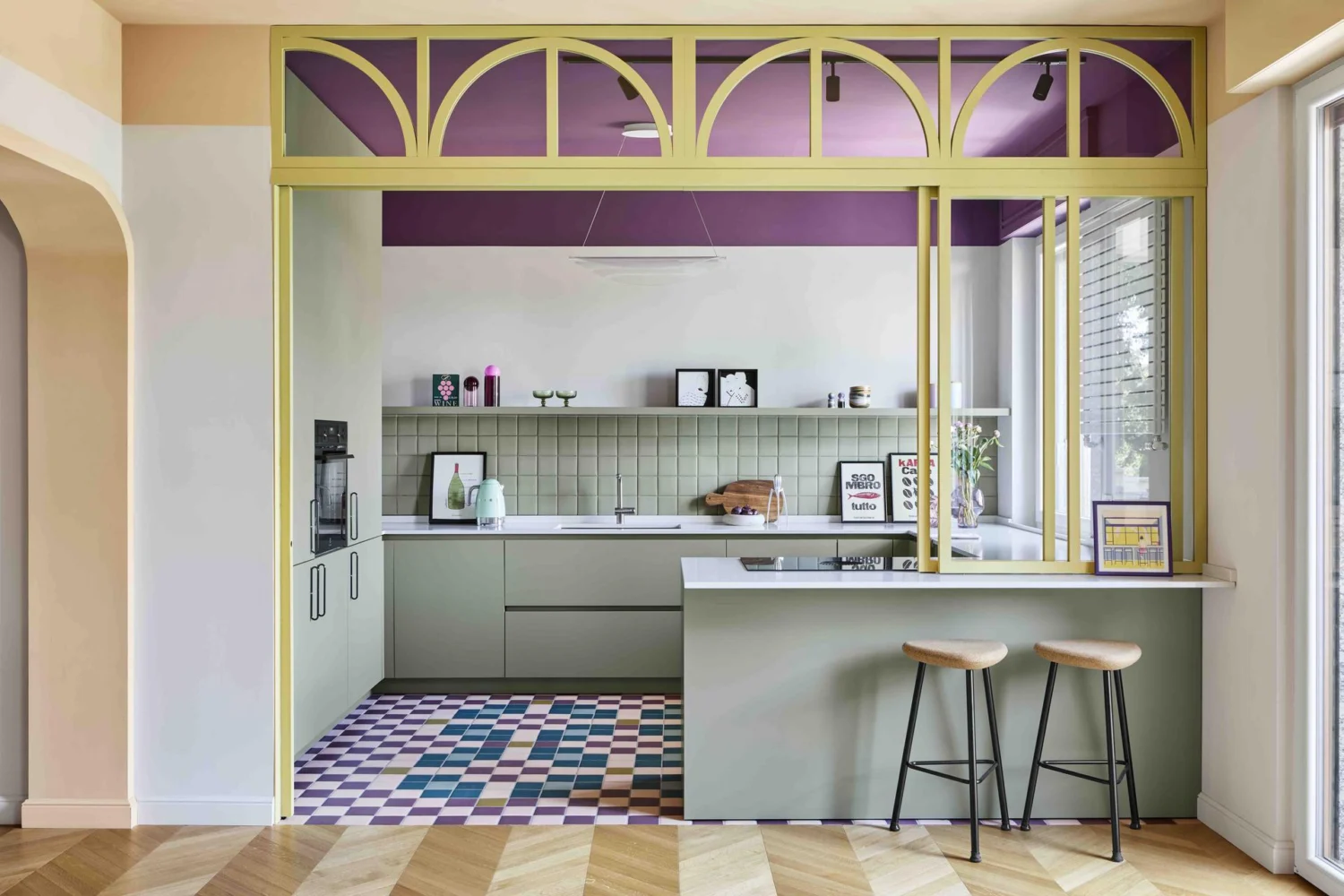 Zona giorno di Residenza B05 a Milano con vetrata ad arcate verde salvia, cucina, soffitto viola e pavimento a mosaico