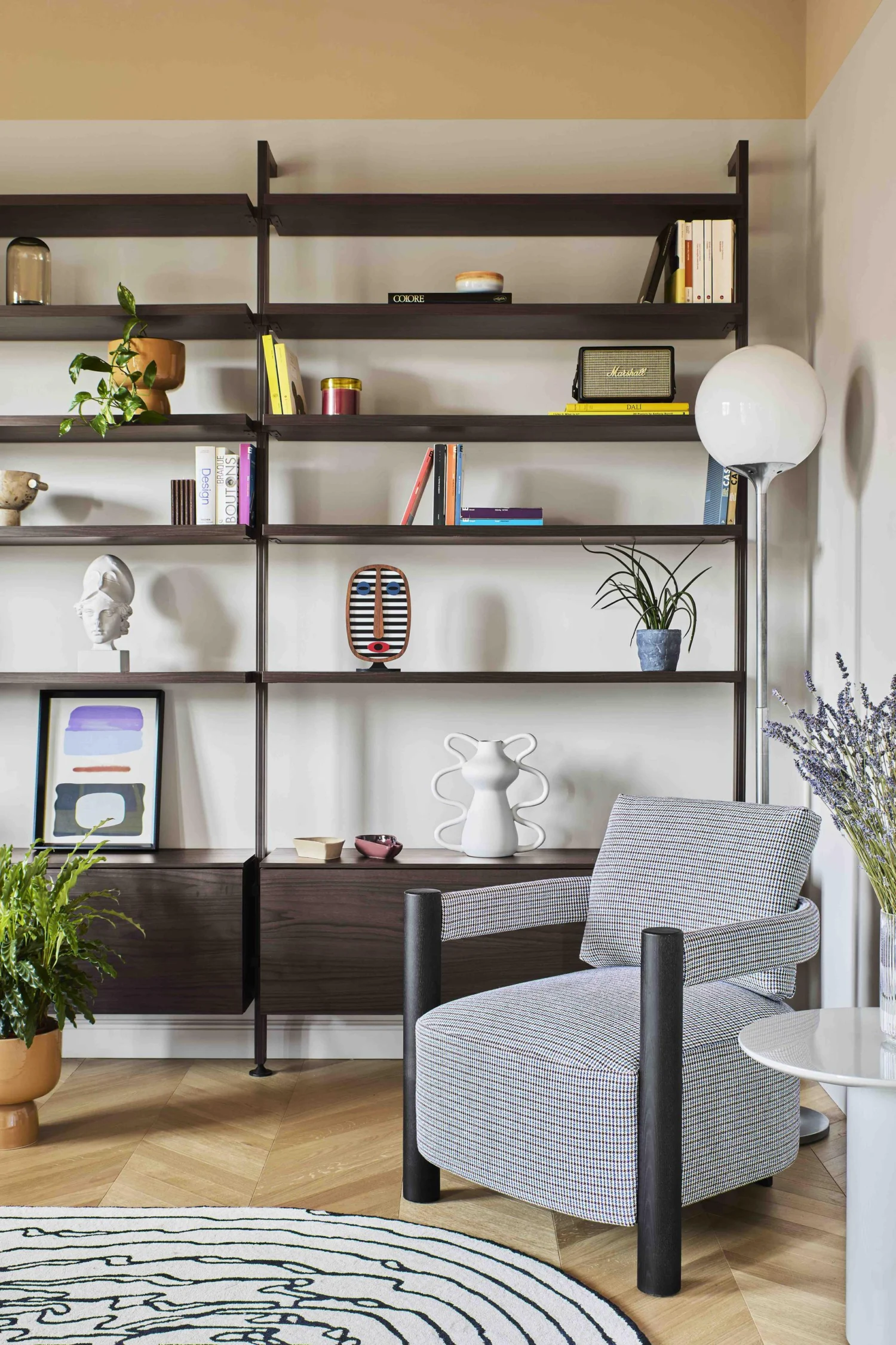 Living di Residenza B05 con libreria a giorno, poltrona in tessuto a motivo grafico, lampada a globo e tappeto tondo