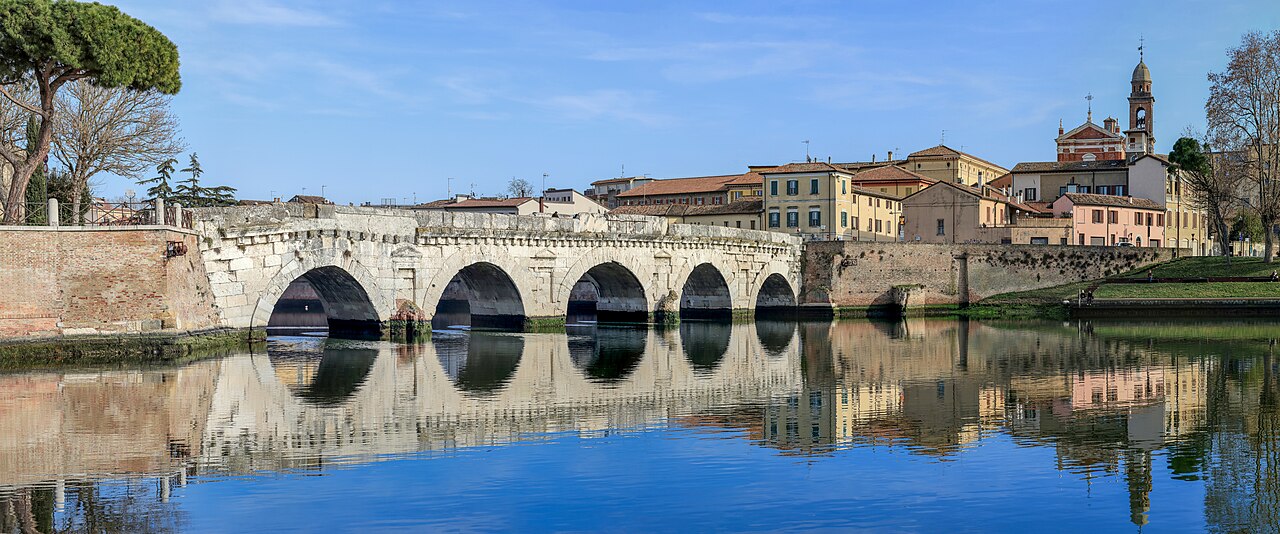 Le cinque arcate del Ponte di Tiberio a Rimini riflesse nell’acqua, con il centro storico sullo sfondo