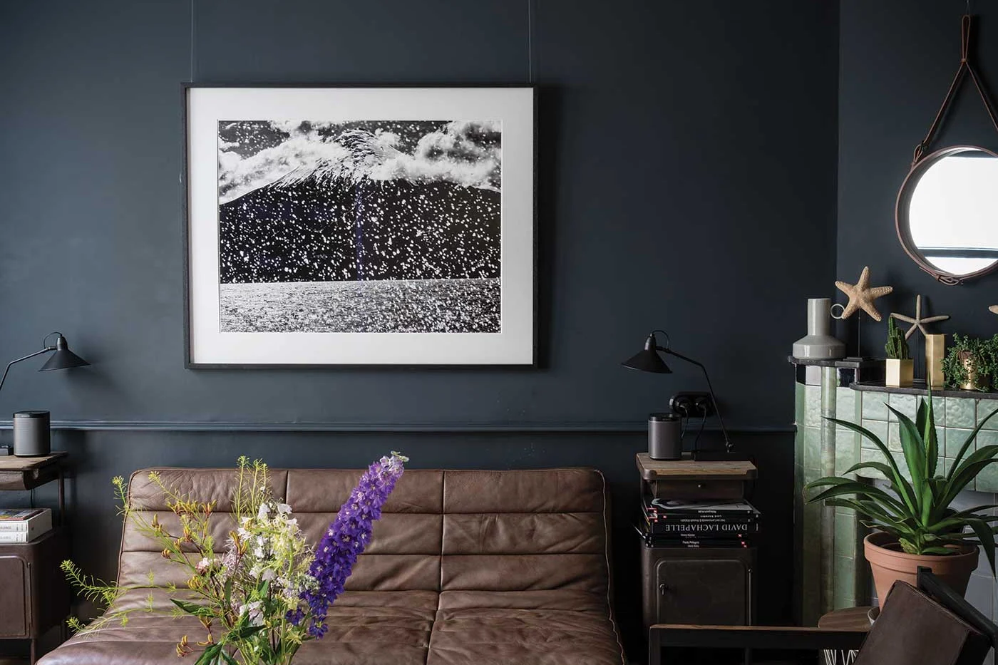 Soggiorno con pareti blu quasi nero, divano in pelle marrone e quadro in bianco e nero