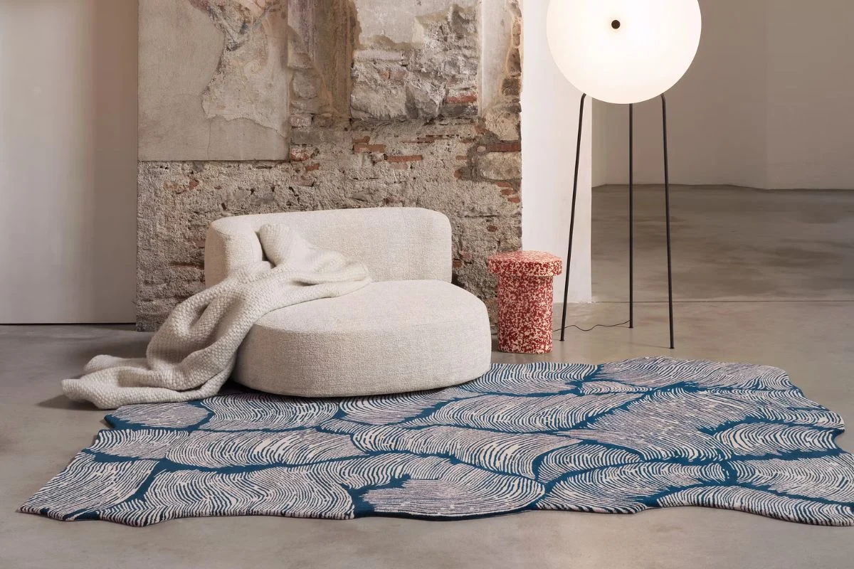 Tappeto dal contorno irregolare con motivo blu e bianco sotto una chaise longue bianca