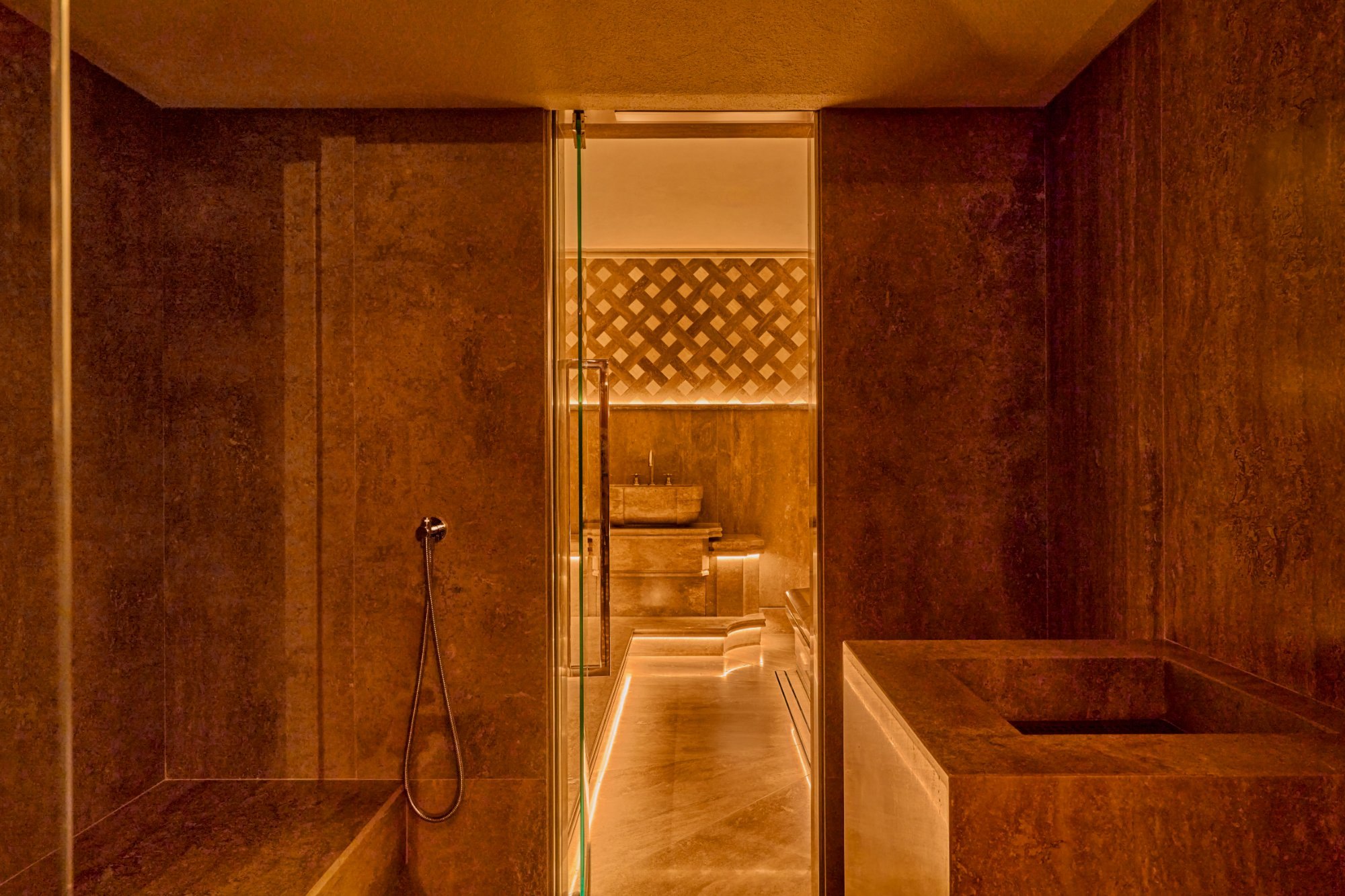 Ambiente rivestito in travertino della spa dell’Orient Express La Minerva a Roma, con porta in vetro e lavabo in pietra sullo sfondo