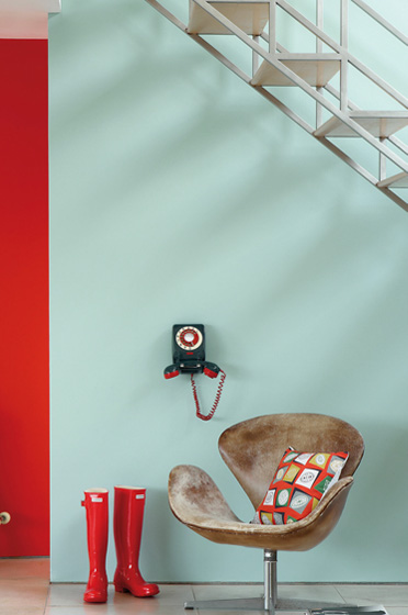 Light blue-green wall with a red door, armchair and white staircase
