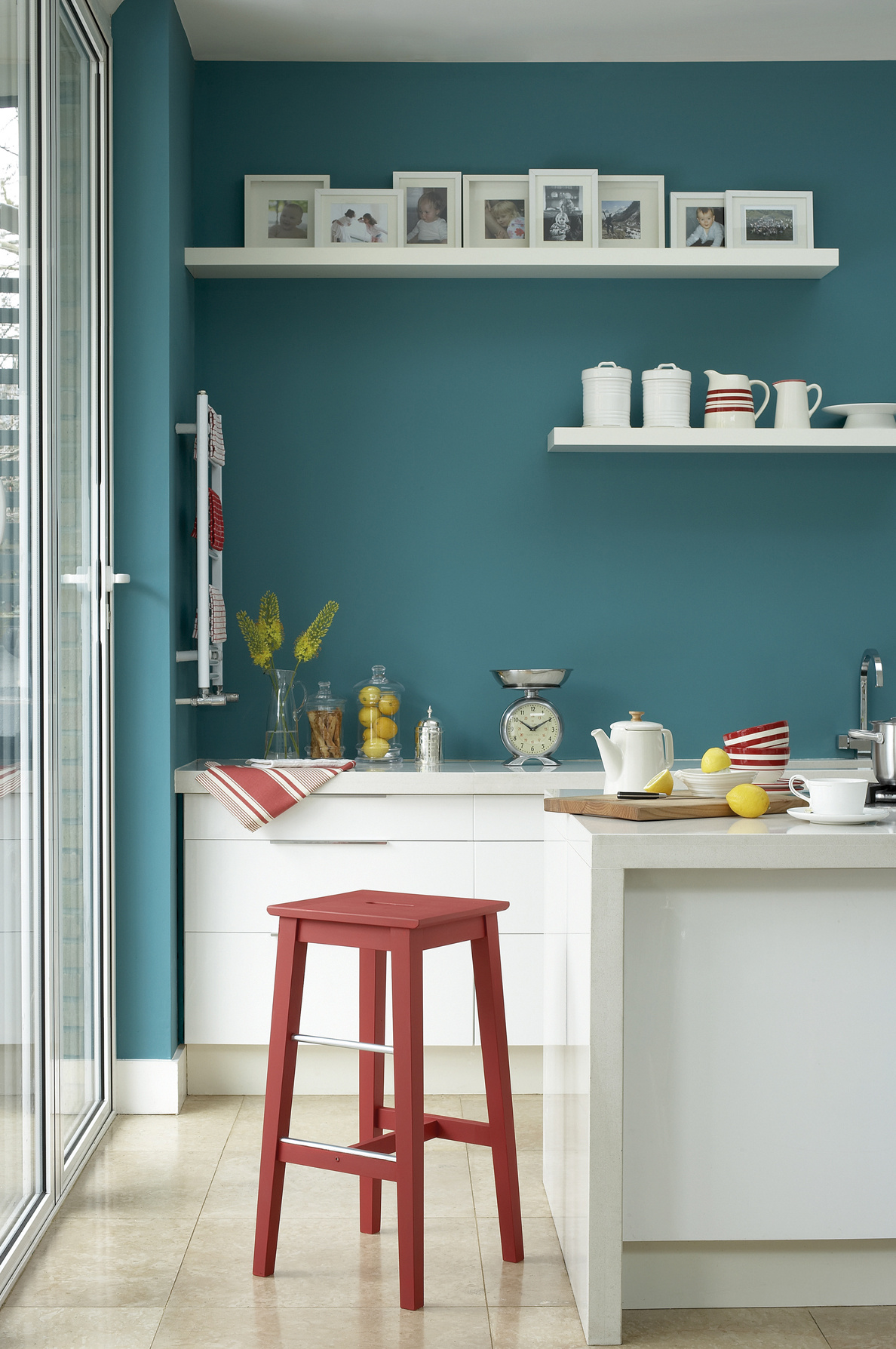 Kitchen with a turquoise wall, white cabinets and red stool